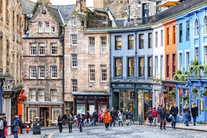 Colorful row of historic buildings and shops on Victoria Street in Edinburgh, Scotland, with people walking along the cobblestone road.
