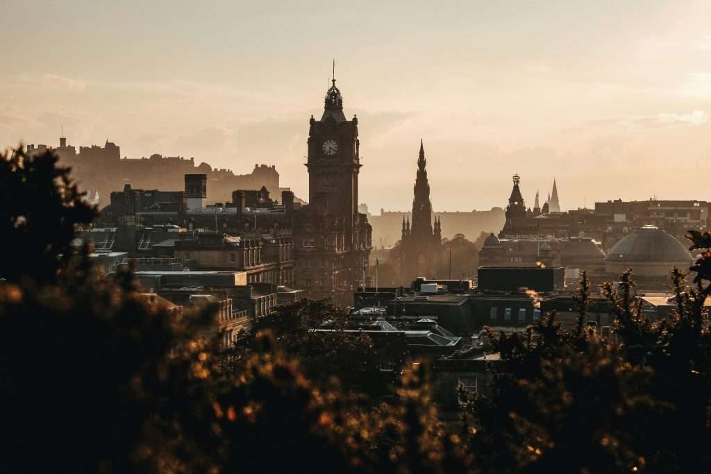 A dramatic silhouette of Edinburgh’s historic skyline at sunset, featuring a prominent clock tower, iconic spires, and warm golden light.