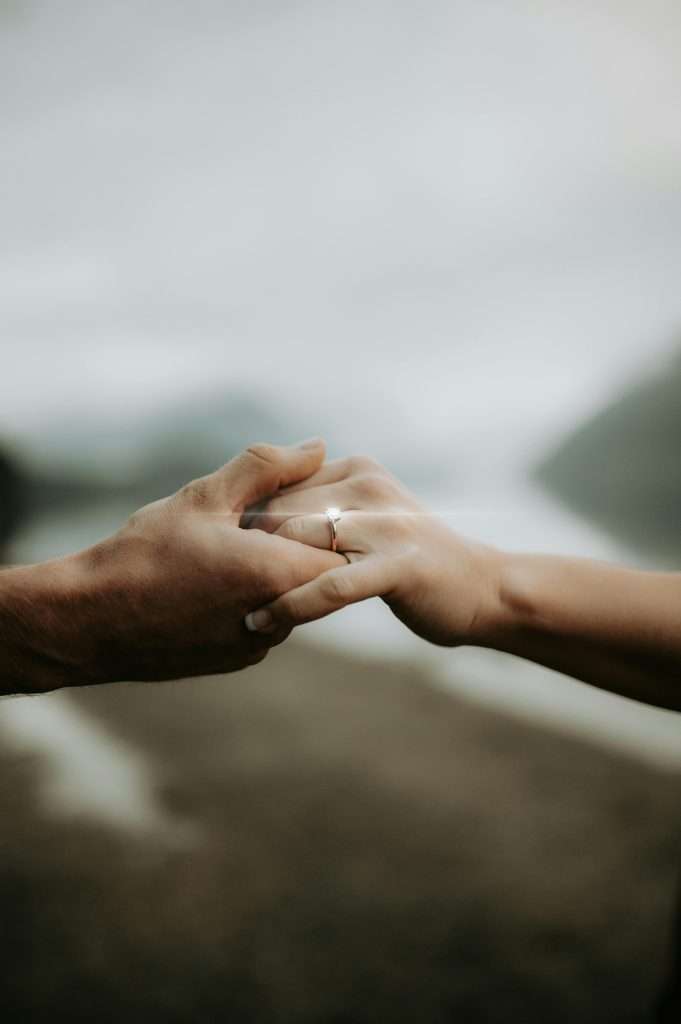 A close-up of two hands gently holding each other, focusing on a sparkling engagement ring and conveying a sense of intimacy and romance.