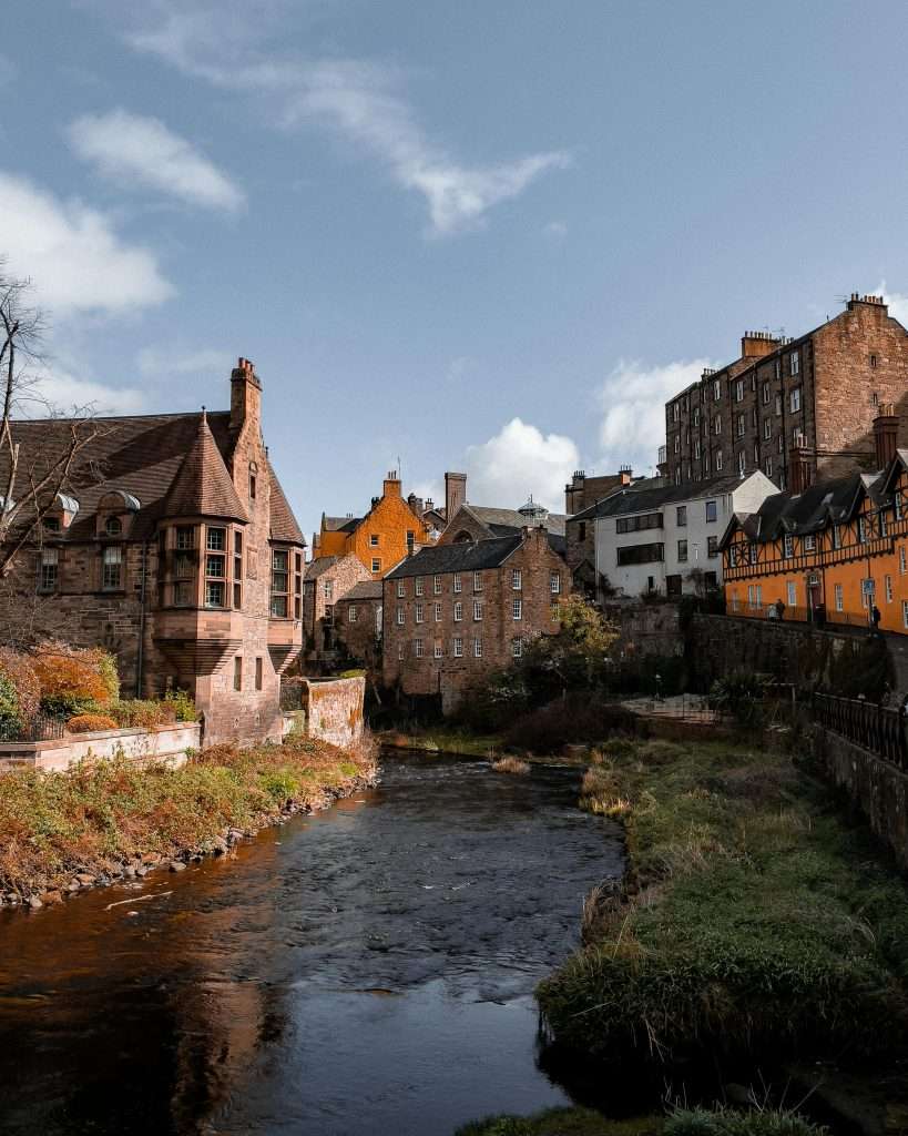A picturesque riverside scene in Edinburgh’s historic Dean Village, featuring charming stone buildings with vibrant façades set along the gentle flow of the Water of Leith.