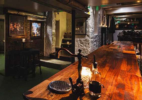 Rustic interior with long wooden bar, candles, stone walls, and dim lighting.