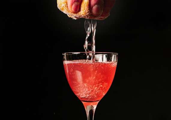 Cocktail glass with pink drink, fresh juice squeezed from a sponge above.