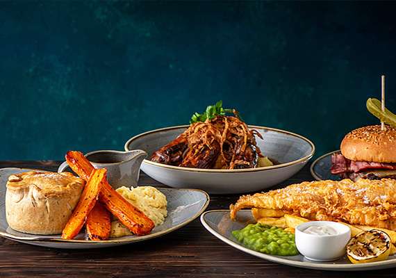 Three plates of British pub food including pie, carrots, mash, burger, and fish and chips.