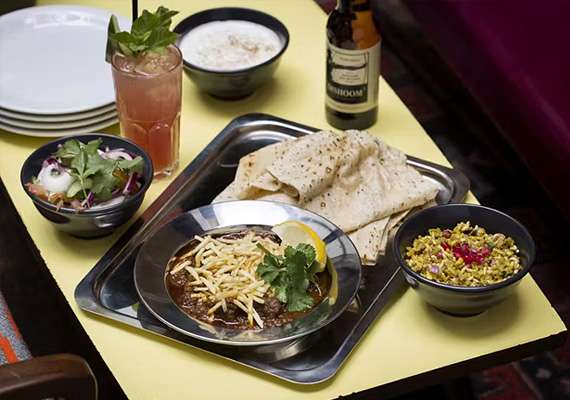 Tray of Indian dishes served with flatbread, salad, rice, and refreshing beverage.