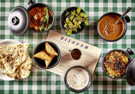 Indian feast with curry, rice, naan, samosas, and chutney on a green-checkered table.