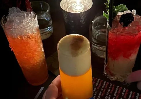 Trio of vibrant cocktails on a dark table with crushed ice, foam, and candlelight.