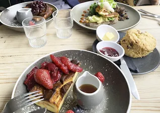 French toast topped with strawberries and syrup, scone with jam and avocado toast in background