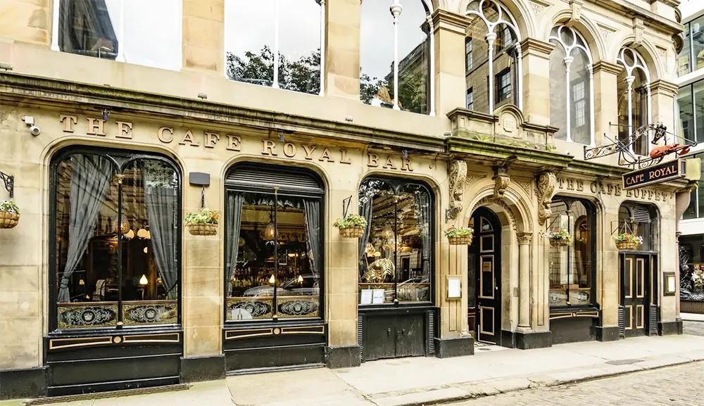 Café Royal Bar exterior with ornate windows and hanging flower baskets on stone facade
