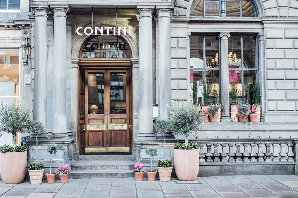 Elegant stone building with wooden double doors, potted plants, and "CONTINI" sign above entrance.