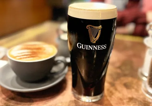 Guinness beer and cappuccino on wooden table in warmly lit café or pub setting