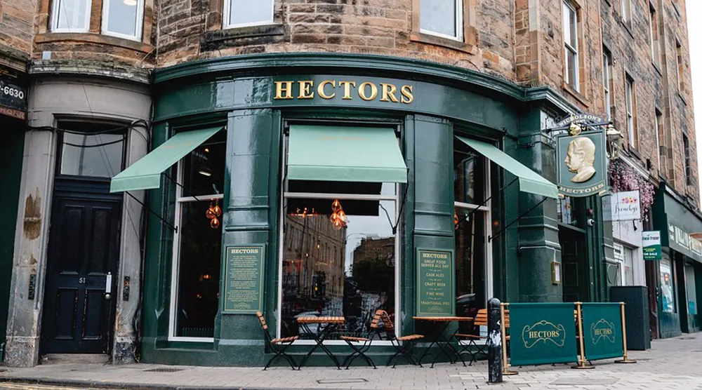 Green-painted corner pub with gold lettering, outdoor tables, and awnings on Stockbridge street.