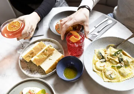 Fresh ravioli with sage butter, focaccia bread, olive oil dip, and cocktails on marble table.