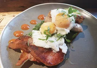 Poached egg and crispy bacon on sourdough toast with microgreens and sauce dots