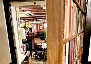 Partially open bookshelf door revealing warm pub interior with wooden beams and leather chairs.