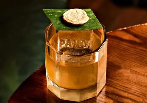 Golden cocktail in crystal glass with leaf and biscuit garnish on wooden table.
