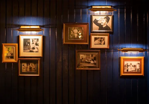 Framed vintage photographs on dark wood‑paneled wall under picture lights