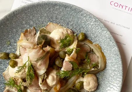 Thinly sliced veal with tuna sauce, capers, and fresh dill on a textured ceramic plate.