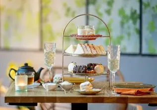 Afternoon tea stand with sandwiches, pastries, champagne flutes and teapot on table.