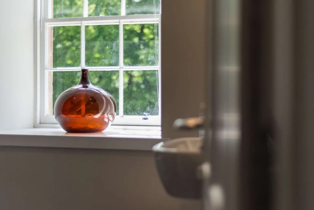 Amber glass vase placed on a white window sill with sunlight and green trees outside