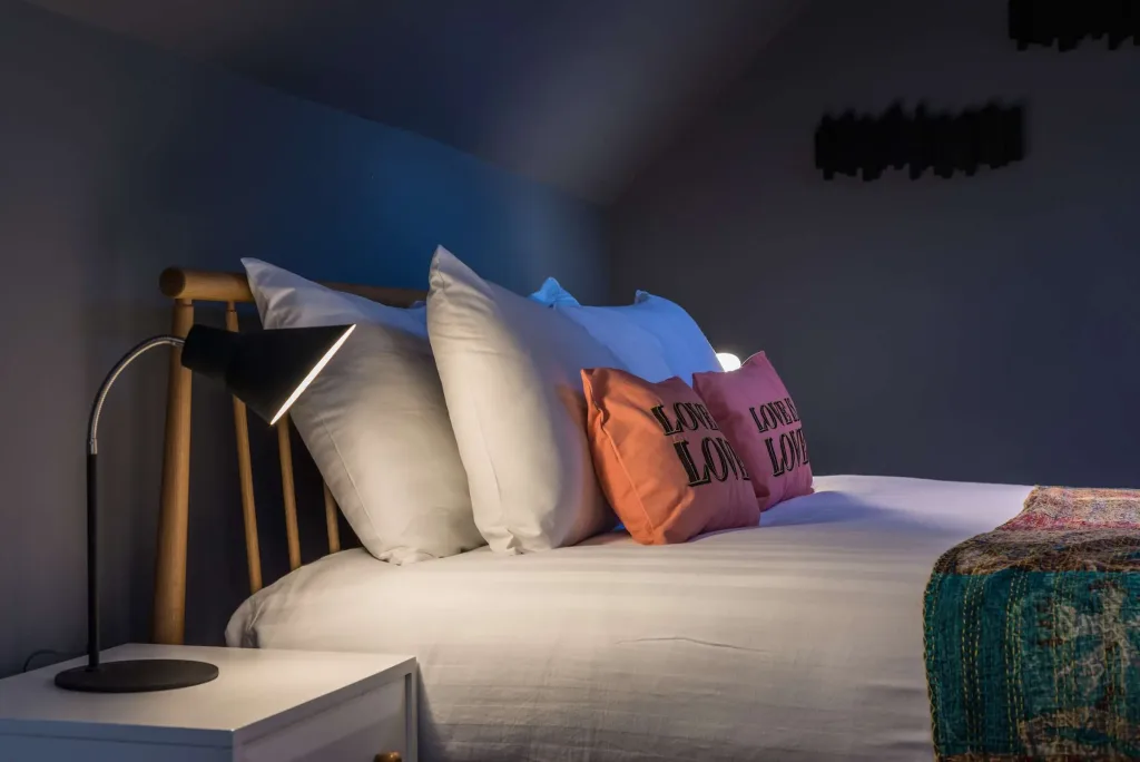 Close-up of bedside lamp, white pillows, and decorative cushions on double bed