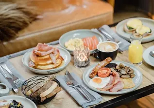 Breakfast table with full English plate, pancakes with bacon, coffee and orange juice.