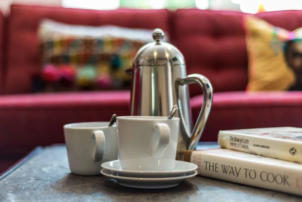 Coffee cups with French press and cookbooks on a table in cottage living room