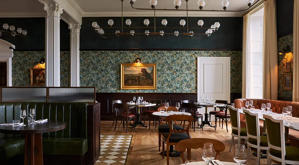 Elegant restaurant dining room with chandeliers, white columns, patterned wallpaper, set tables.