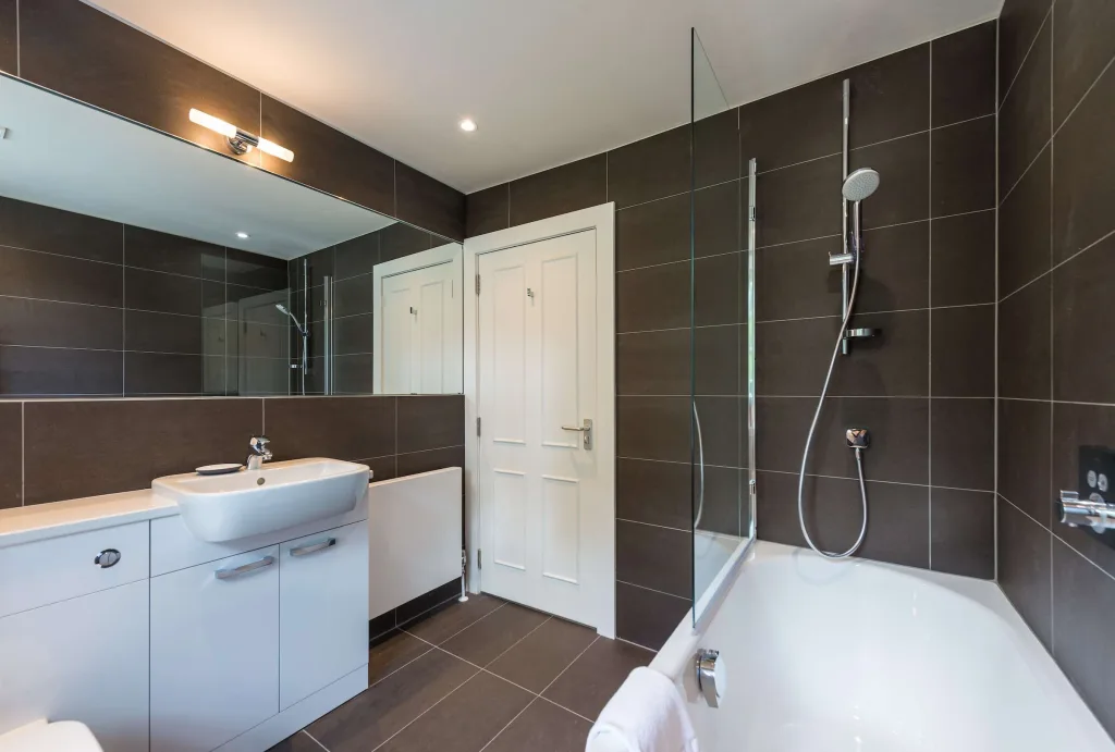 Modern bathroom with bathtub, overhead shower, large mirror, and white sink cabinet