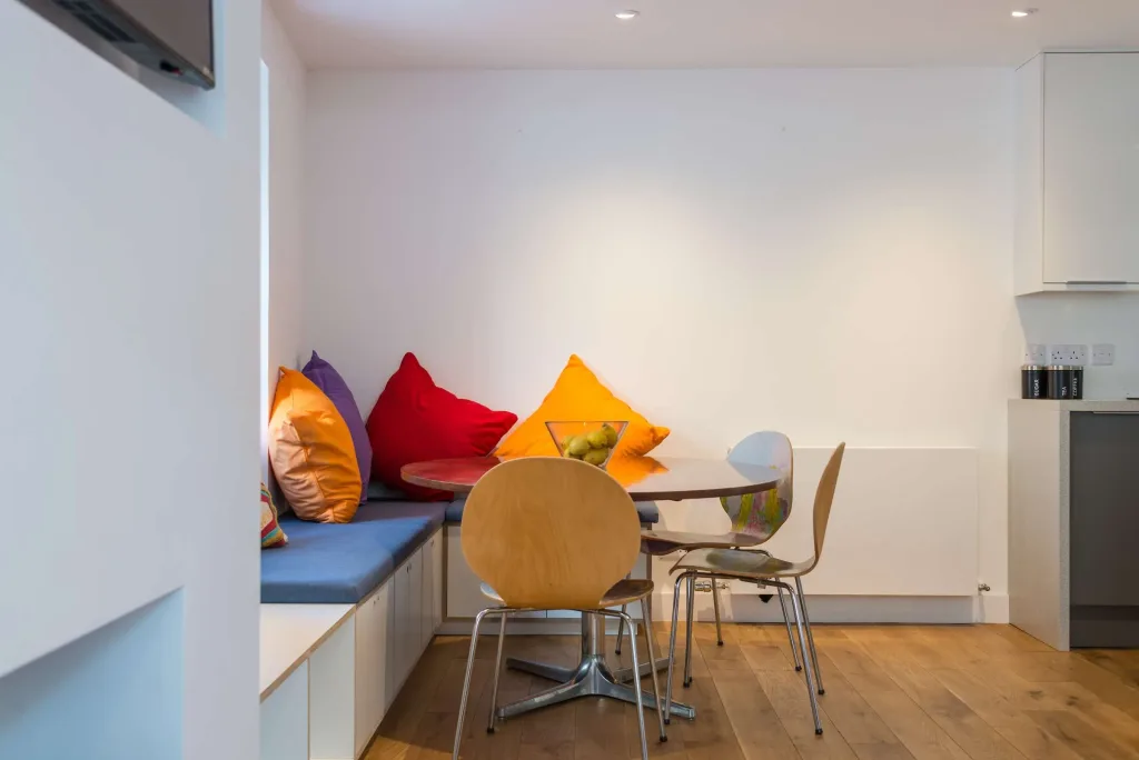 Cozy dining nook with round wooden table, modern chairs, and colourful cushions on a bench seat