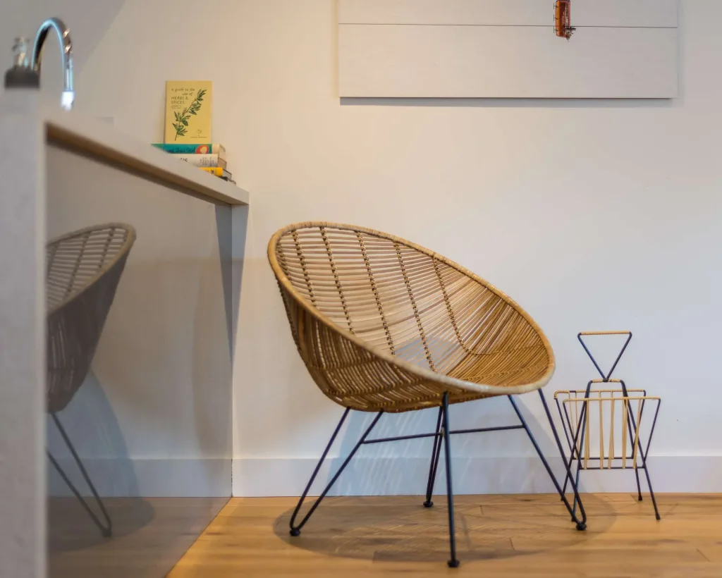 Modern rattan chair with metal legs next to a small magazine holder in a bright living space with wooden floor