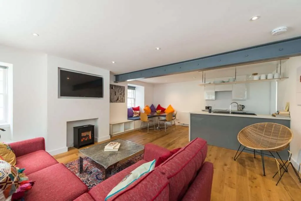 Modern open-plan living room with red sofa, wall-mounted TV, fireplace, dining nook, and kitchen area