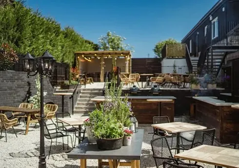 Outdoor garden dining patio with tables, pergola and string lights.