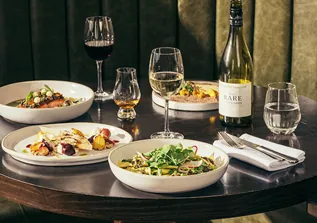 Restaurant table with plated dishes, red and white wine, whisky, and bottle.