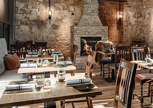Rustic dining room with stone fireplace, exposed walls, wooden tables neatly set.
