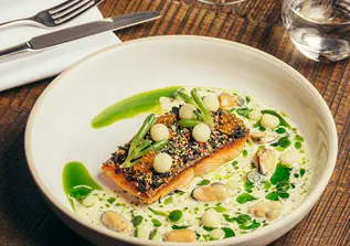 Seared fish with seed crust in creamy shellfish sauce and green herb oil.