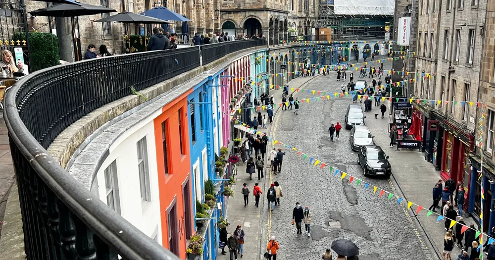 Curved street with colourful buildings, cobblestones, and people walking under bunting flags