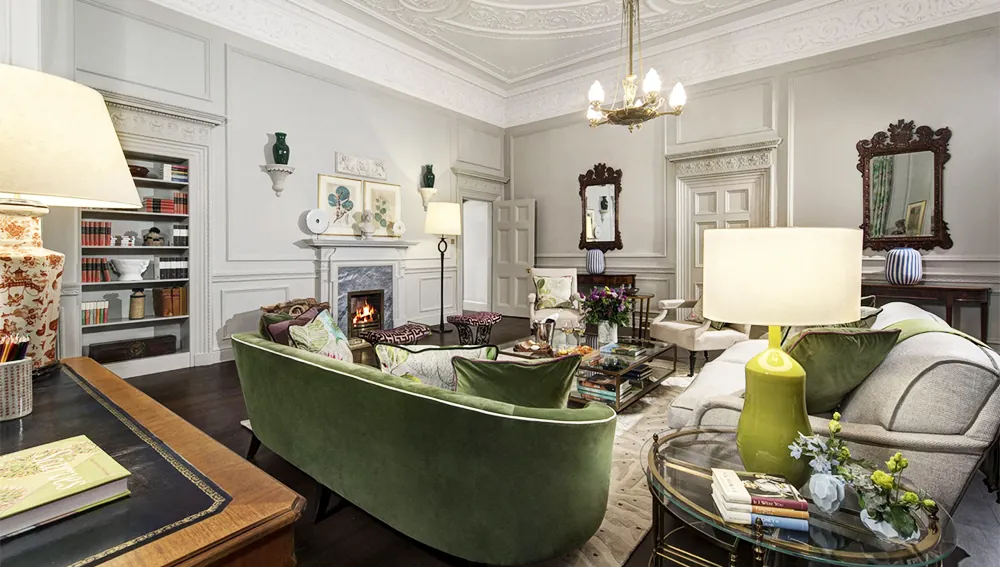 Elegant living room with green velvet sofas, fireplace, chandeliers, and classic ornate ceiling.