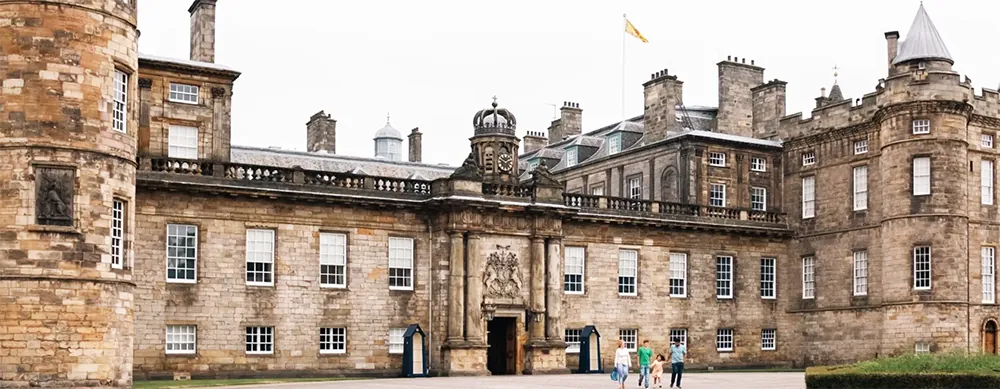 Historic stone palace with towers, arched entrance, and people walking in courtyard.