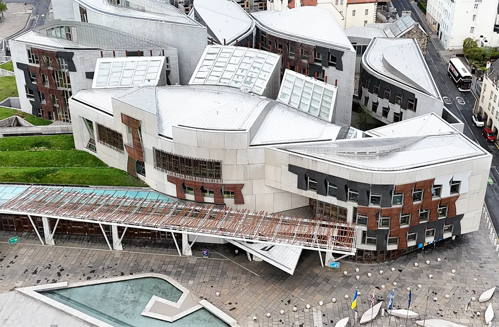 Aerial view of modern building with curved roofs and plaza in front.