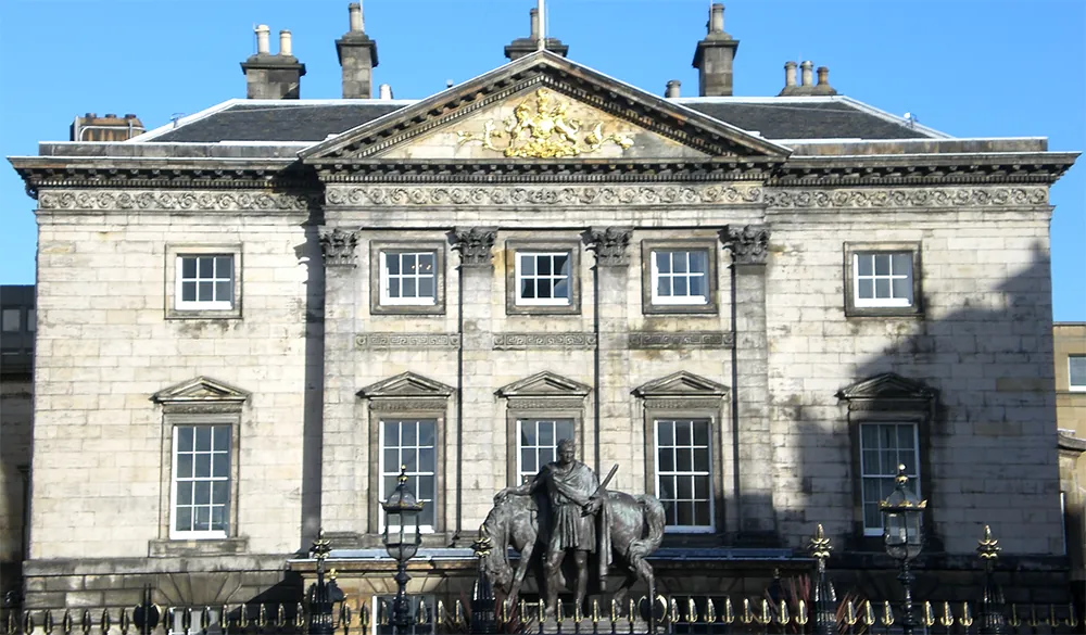 Stone building with symmetrical windows, golden crest, and equestrian statue in front.