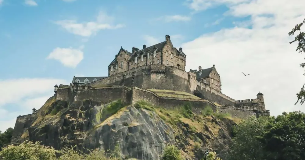 Large stone castle on a rocky hill with blue sky and greenery