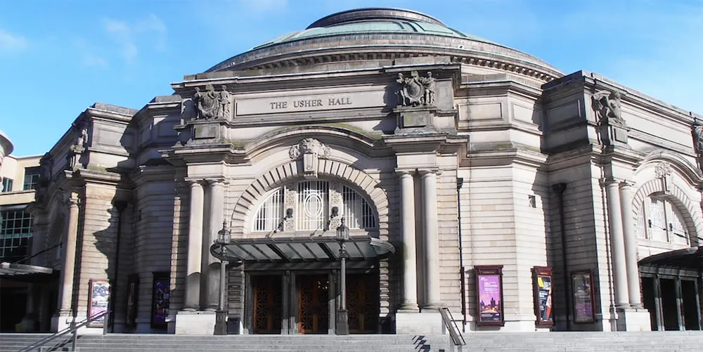 Grand stone concert hall with arched entrance, pillars, and domed roof.